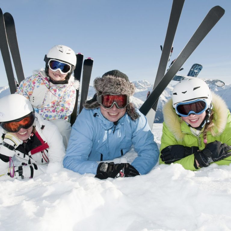 Vier Skifahrer in bunter Winterkleidung posieren auf Schnee vor Bergkulisse.